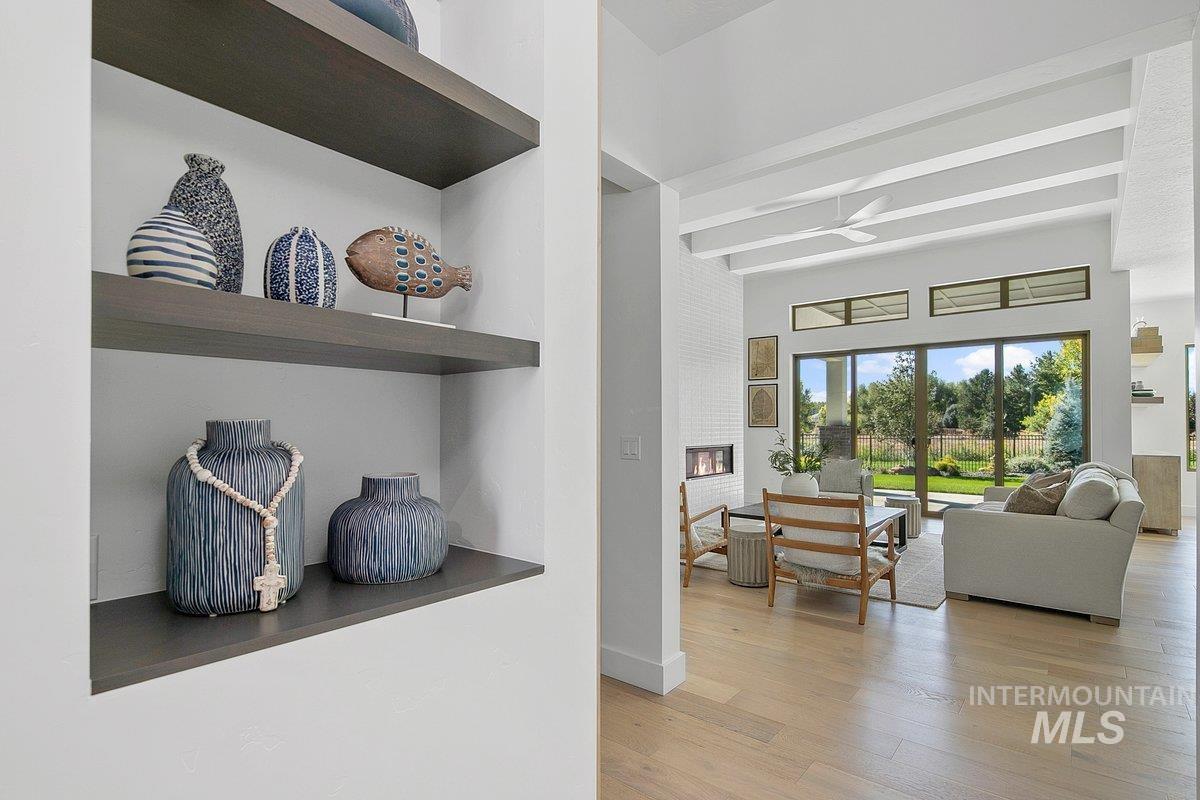Living room with light wood finished floors, a glass covered fireplace, and beamed ceiling