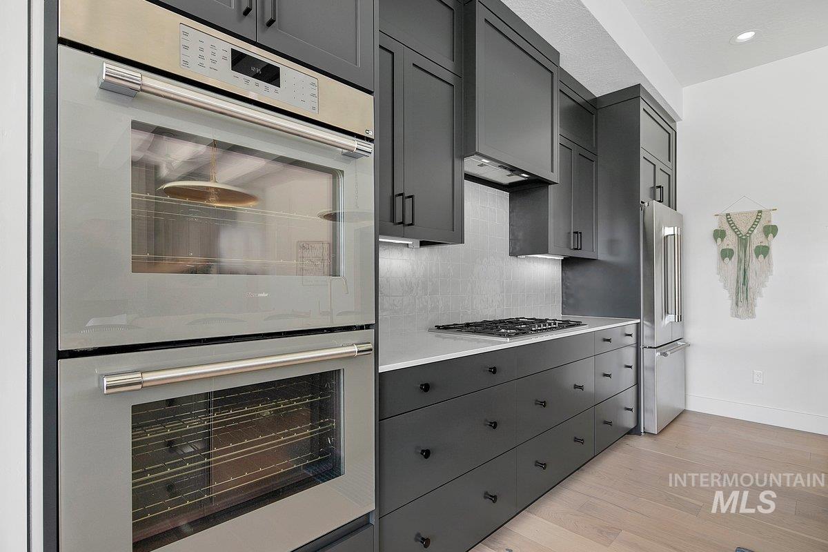 Kitchen featuring stainless steel appliances, gray cabinetry, light wood finished floors, light countertops, and backsplash