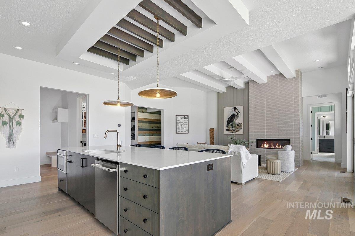 Kitchen with recessed lighting, a large fireplace, hanging light fixtures, an island with sink, and light wood finished floors