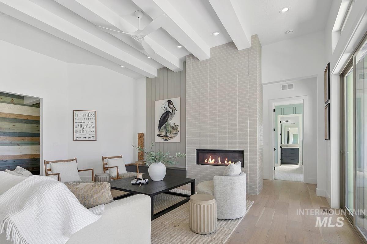 Living room with a tiled fireplace, light wood finished floors, beamed ceiling, and a high ceiling