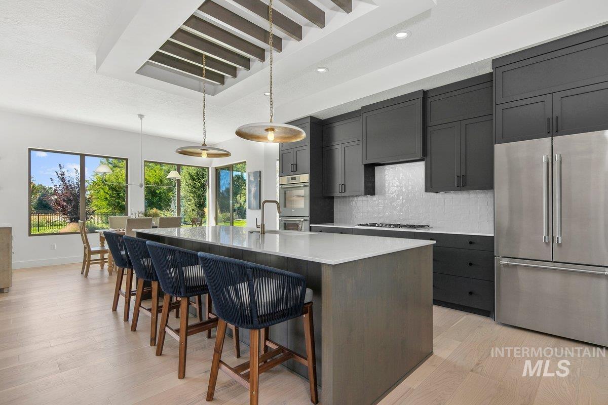 Kitchen featuring decorative backsplash, stainless steel appliances, a kitchen island with sink, light wood-style flooring, and recessed lighting