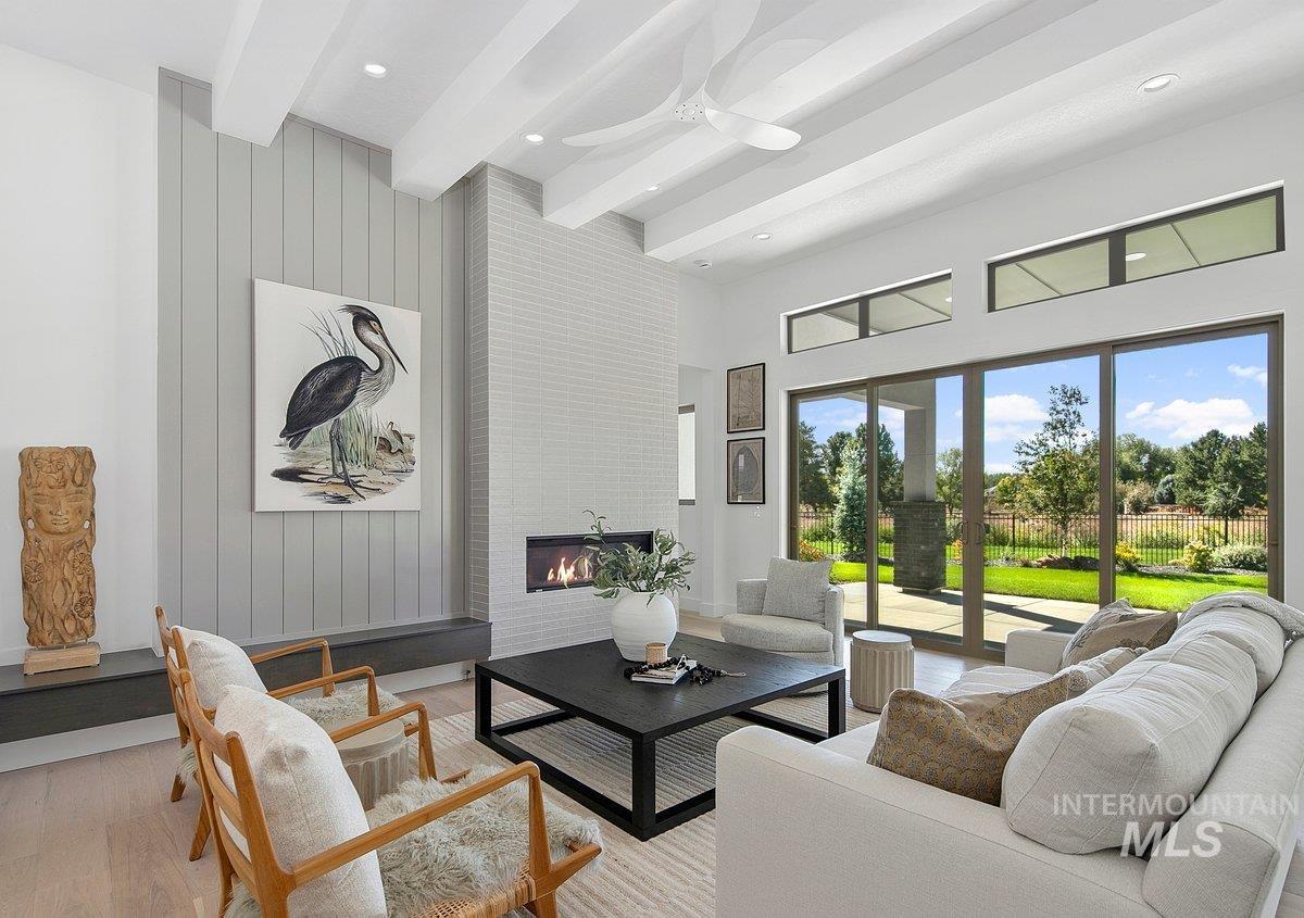 Living room featuring beam ceiling, a fireplace, wood finished floors, a high ceiling, and wooden walls