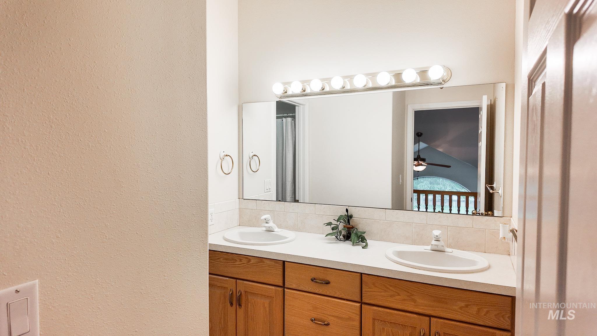 Full bath with double vanity, backsplash, ceiling fan, and a textured wall