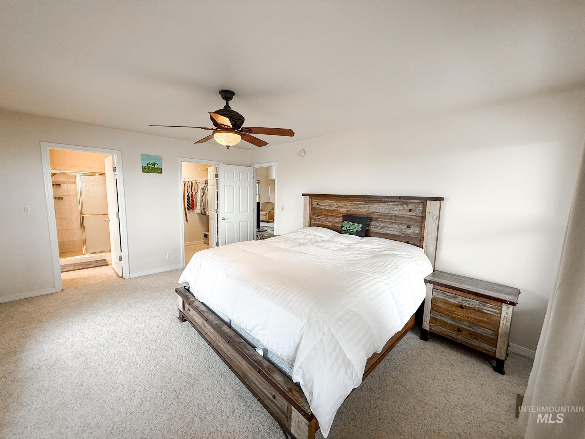 Bedroom with a spacious closet, light colored carpet, ceiling fan, and ensuite bath