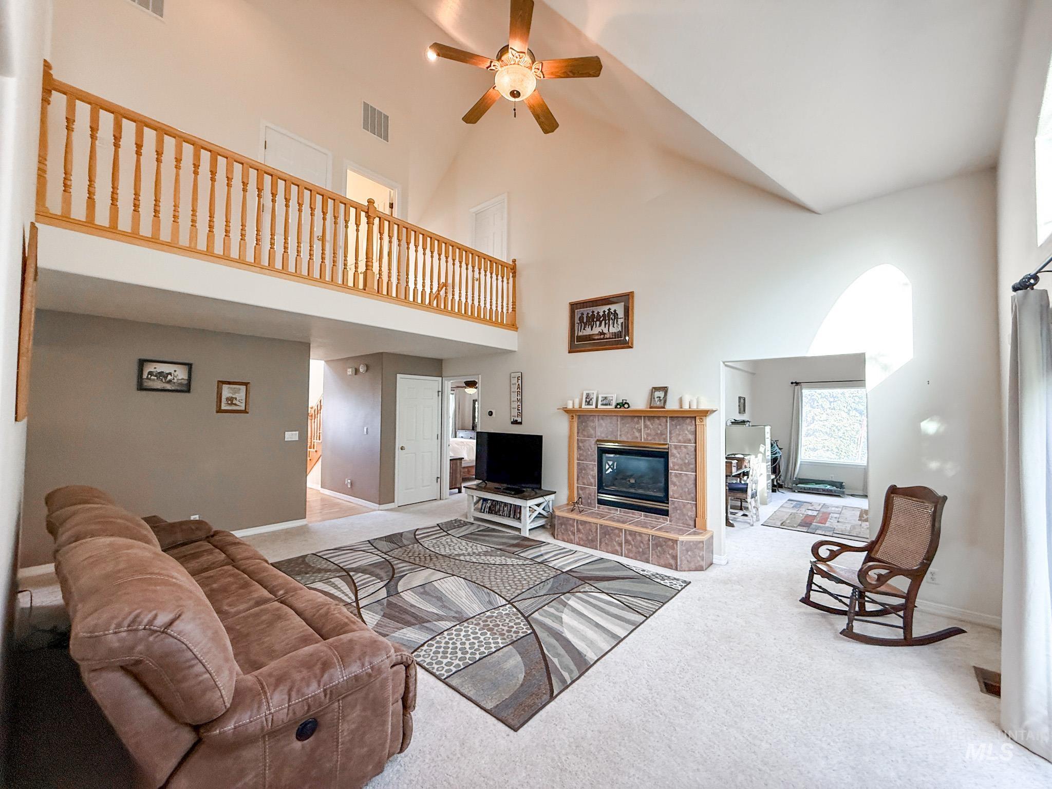 Living area featuring carpet flooring, ceiling fan, a fireplace, and high vaulted ceiling