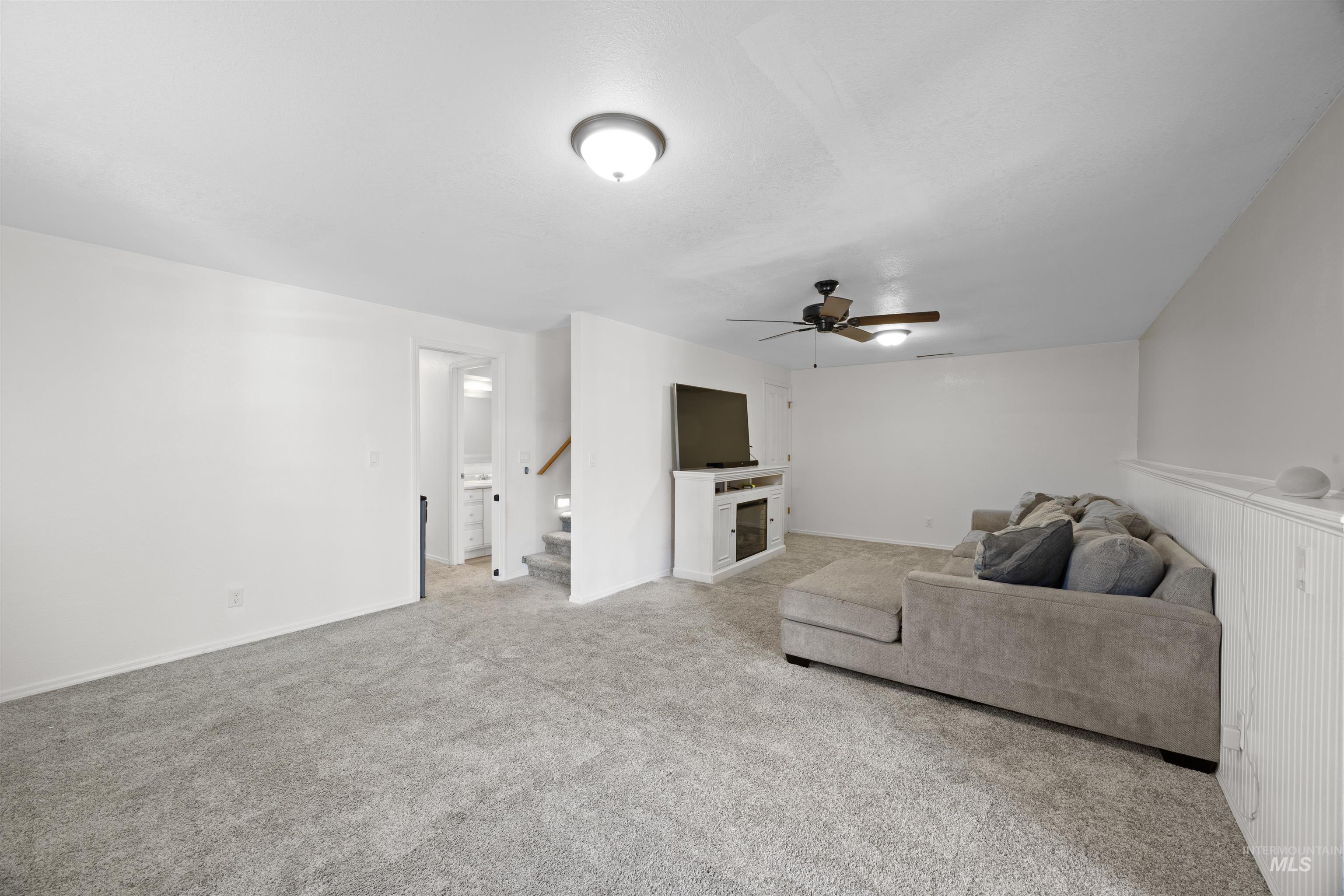 Carpeted living area with a fireplace, stairs, and ceiling fan