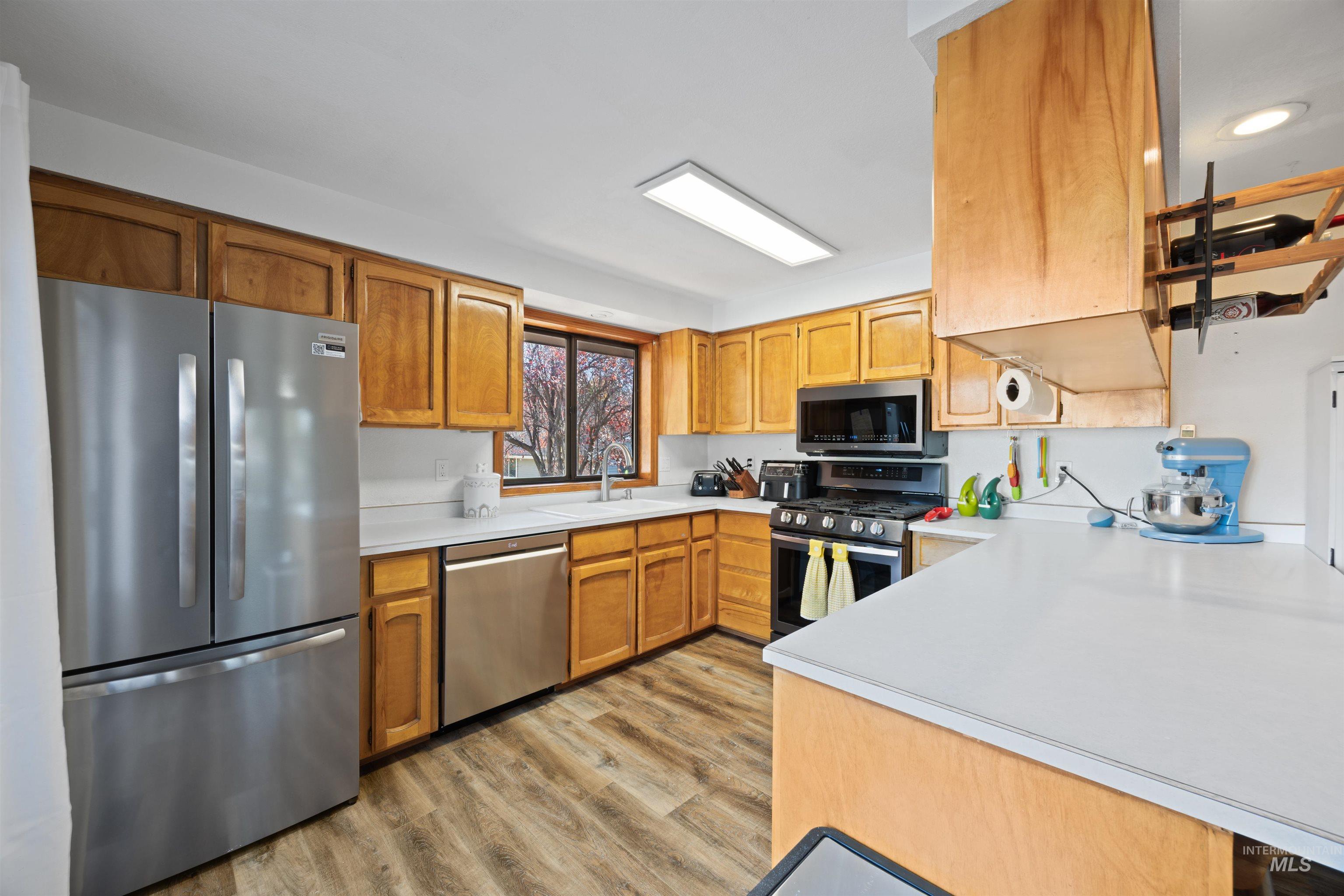 Kitchen featuring stainless steel appliances, light countertops, light wood-style floors, and brown cabinets