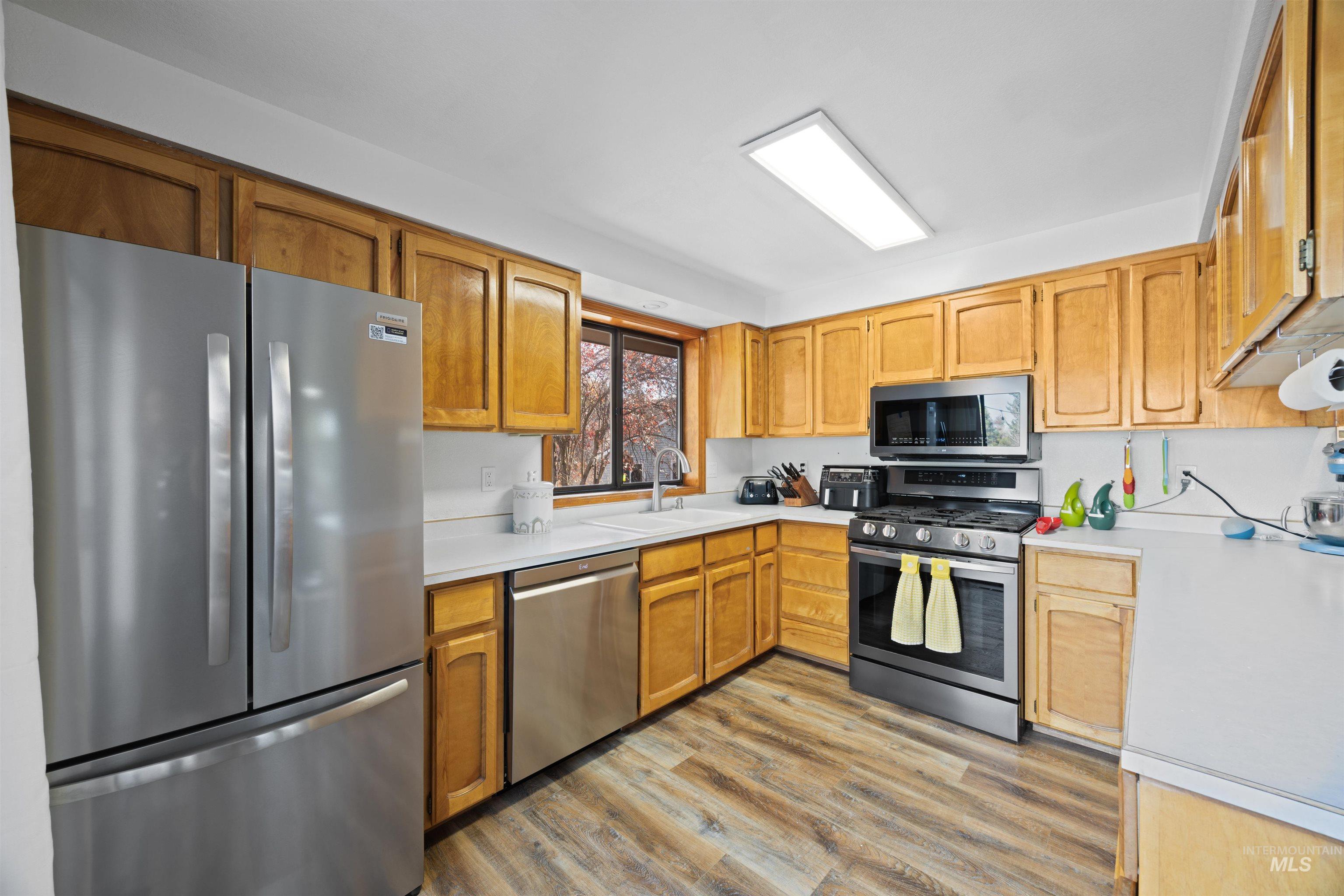 Kitchen featuring appliances with stainless steel finishes, light countertops, light wood-style floors, and brown cabinets