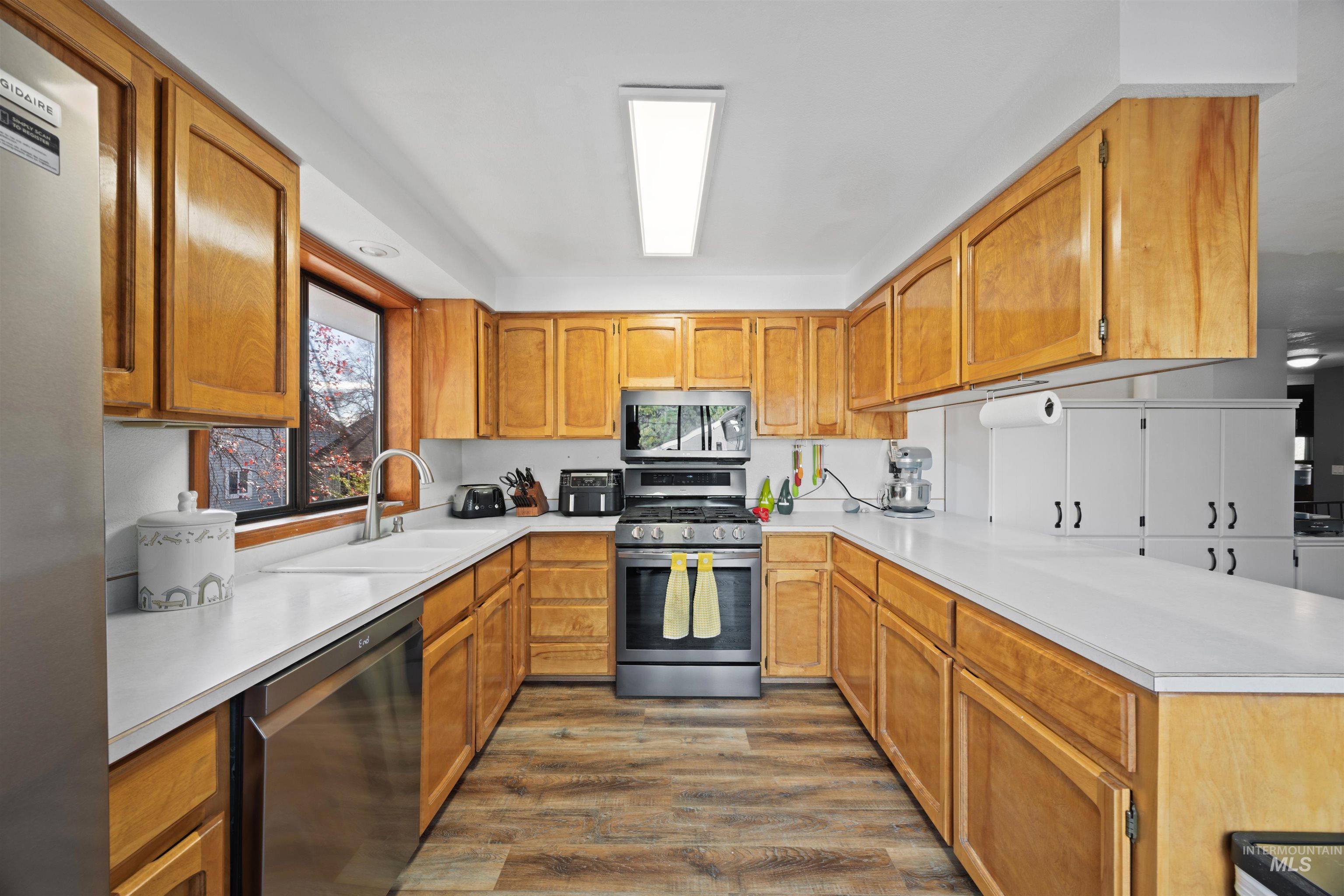Kitchen featuring stainless steel appliances, light countertops, dark wood-style floors, brown cabinets, and a peninsula