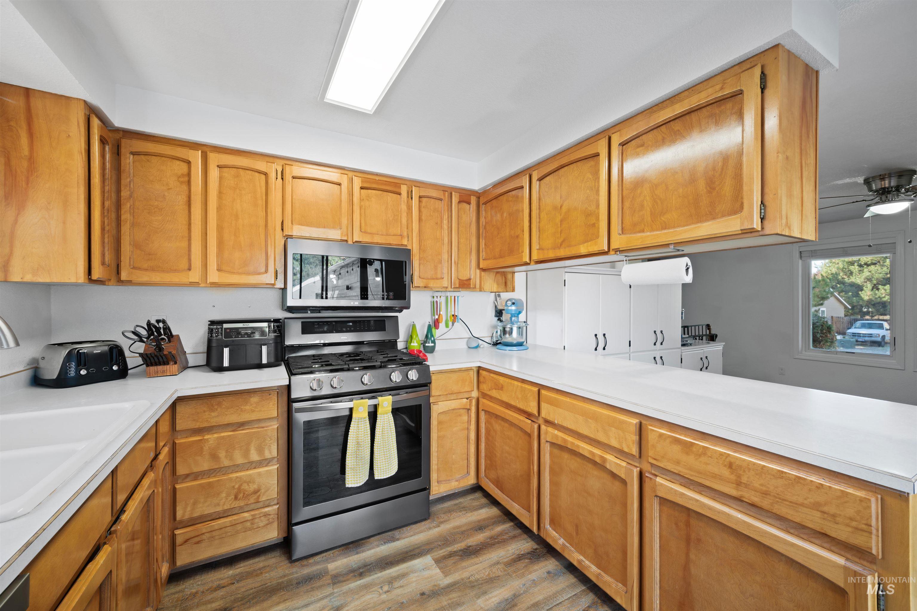 Kitchen featuring light countertops, stainless steel appliances, dark wood-type flooring, and brown cabinets