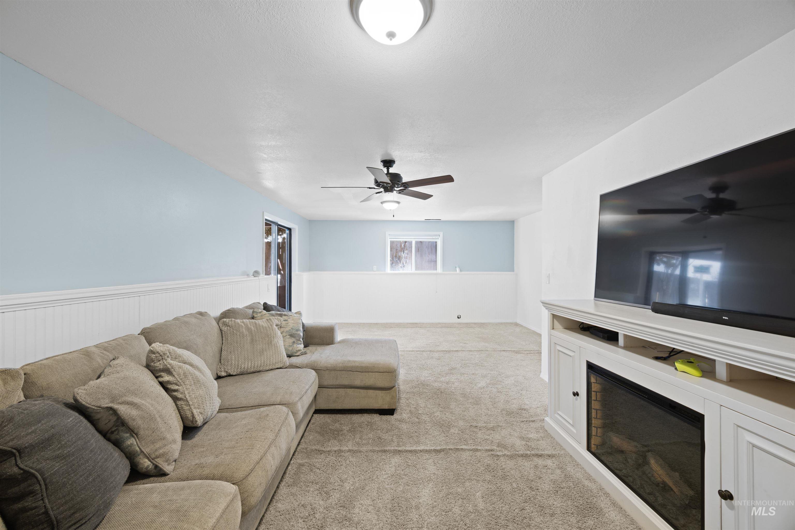 Living room with a glass covered fireplace, light colored carpet, and ceiling fan