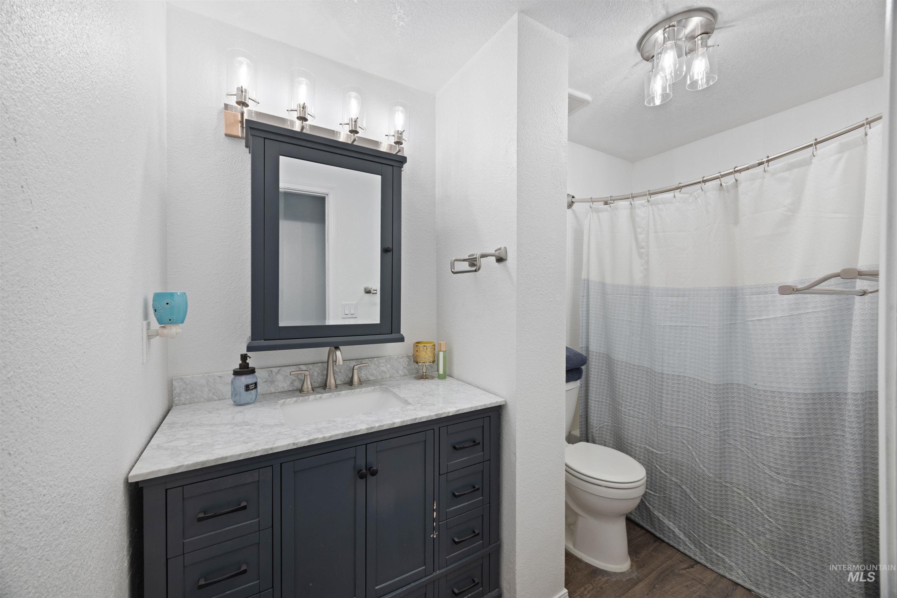 Full bath featuring dark wood-style flooring, vanity, curtained shower, a textured wall, and a textured ceiling