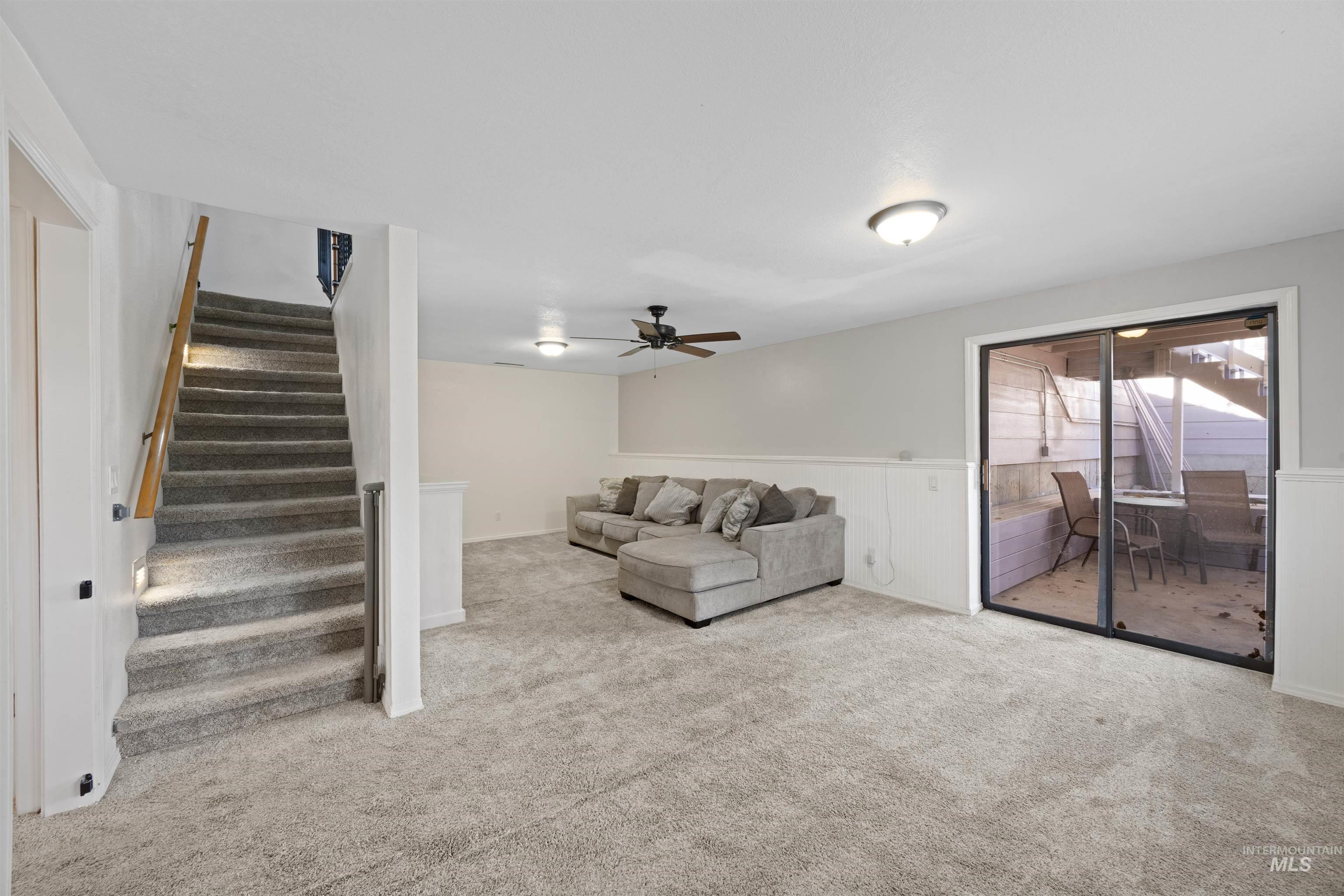 Living area featuring carpet flooring, stairs, and ceiling fan