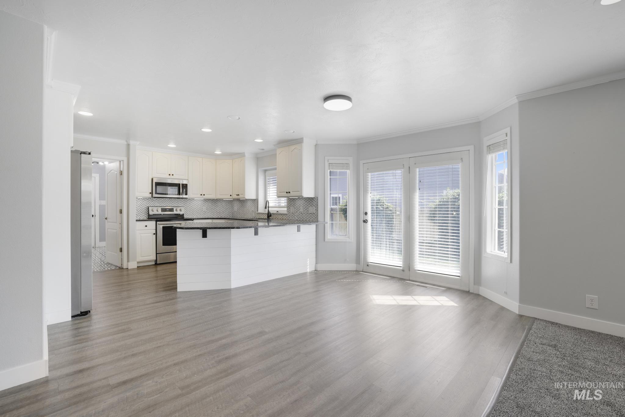 Kitchen featuring crown molding, light wood finished floors, stainless steel appliances, open floor plan, and decorative backsplash