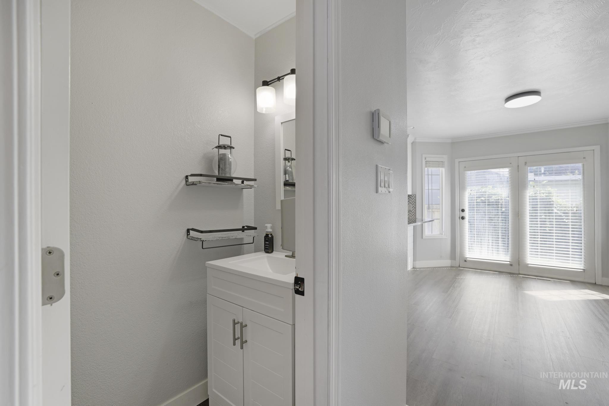 Half bath featuring vanity, crown molding, wood finished floors, and a textured wall