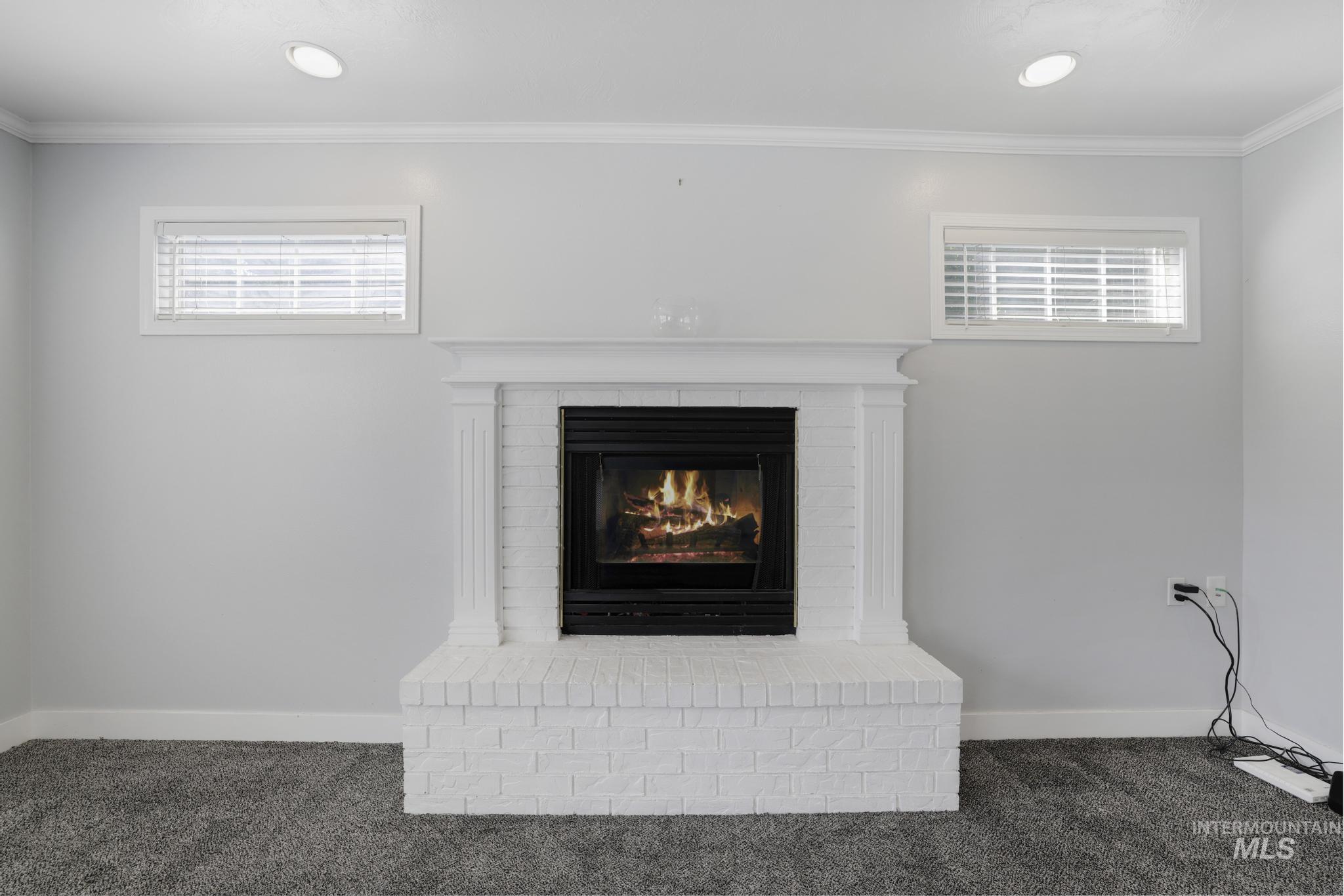 Detailed view of crown molding, carpet flooring, and a brick fireplace