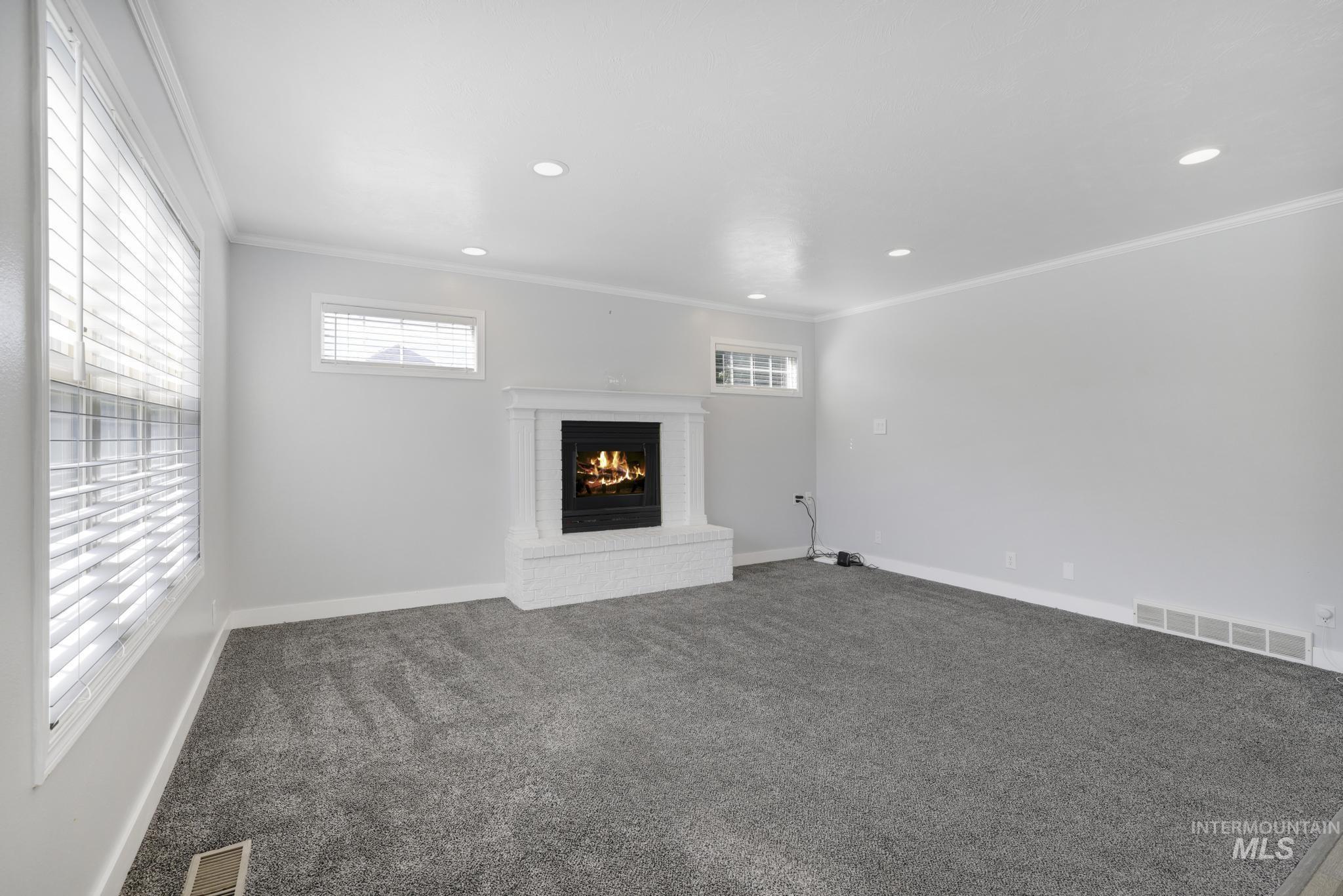 Unfurnished living room featuring crown molding, carpet, a brick fireplace, and recessed lighting