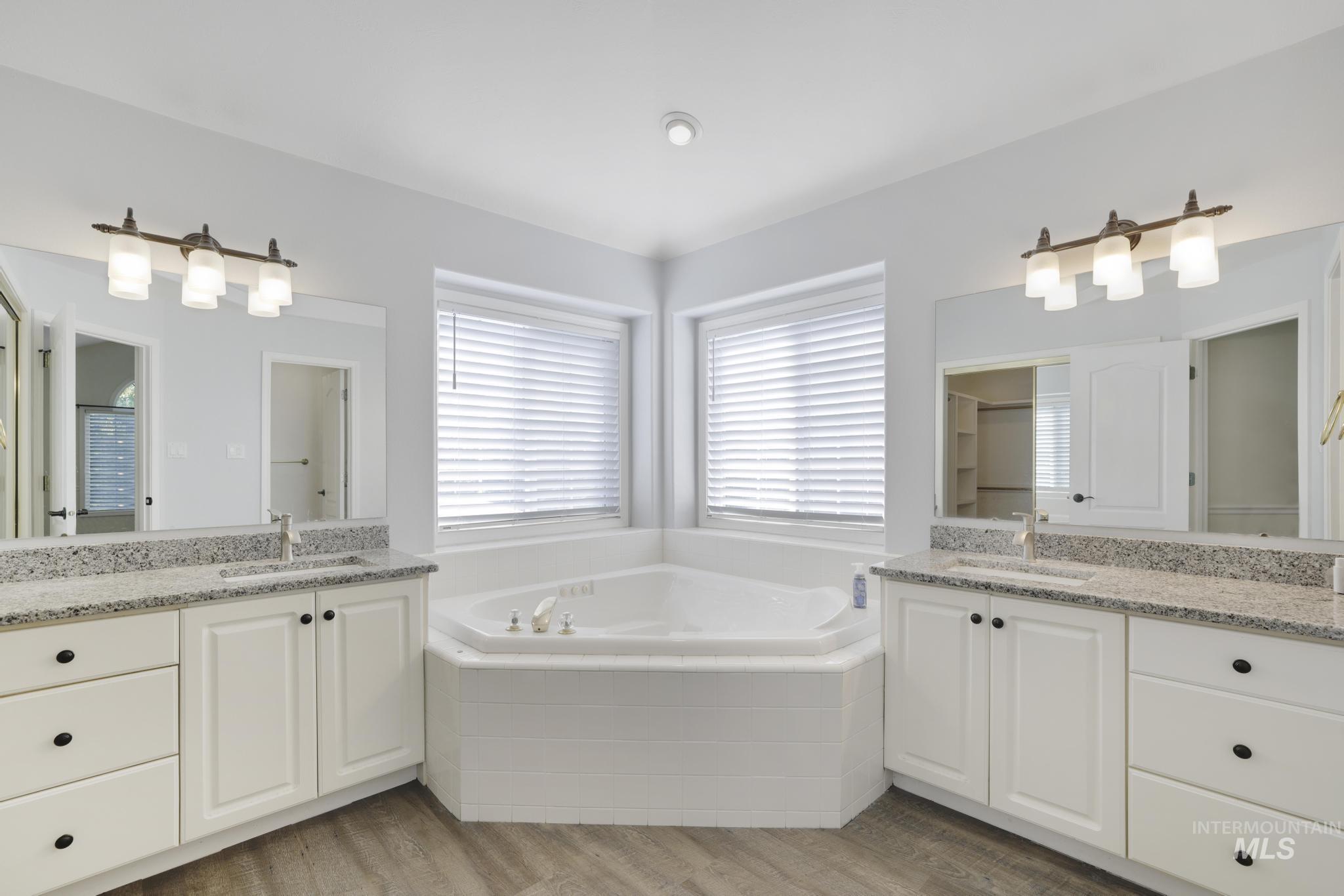 Bathroom with two vanities, a bath, and light wood finished floors