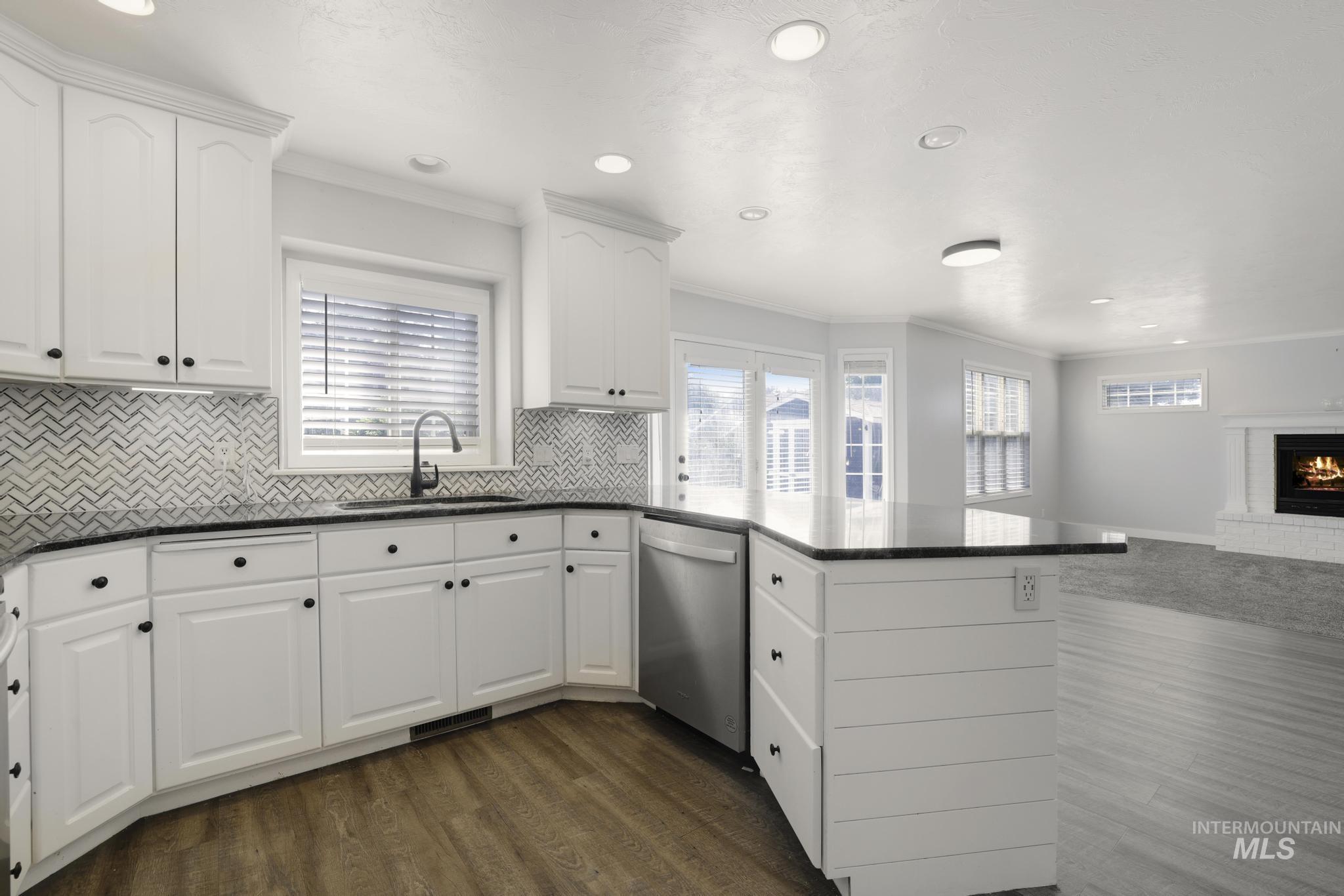 Kitchen with a peninsula, ornamental molding, open floor plan, white cabinets, and dark wood-style flooring