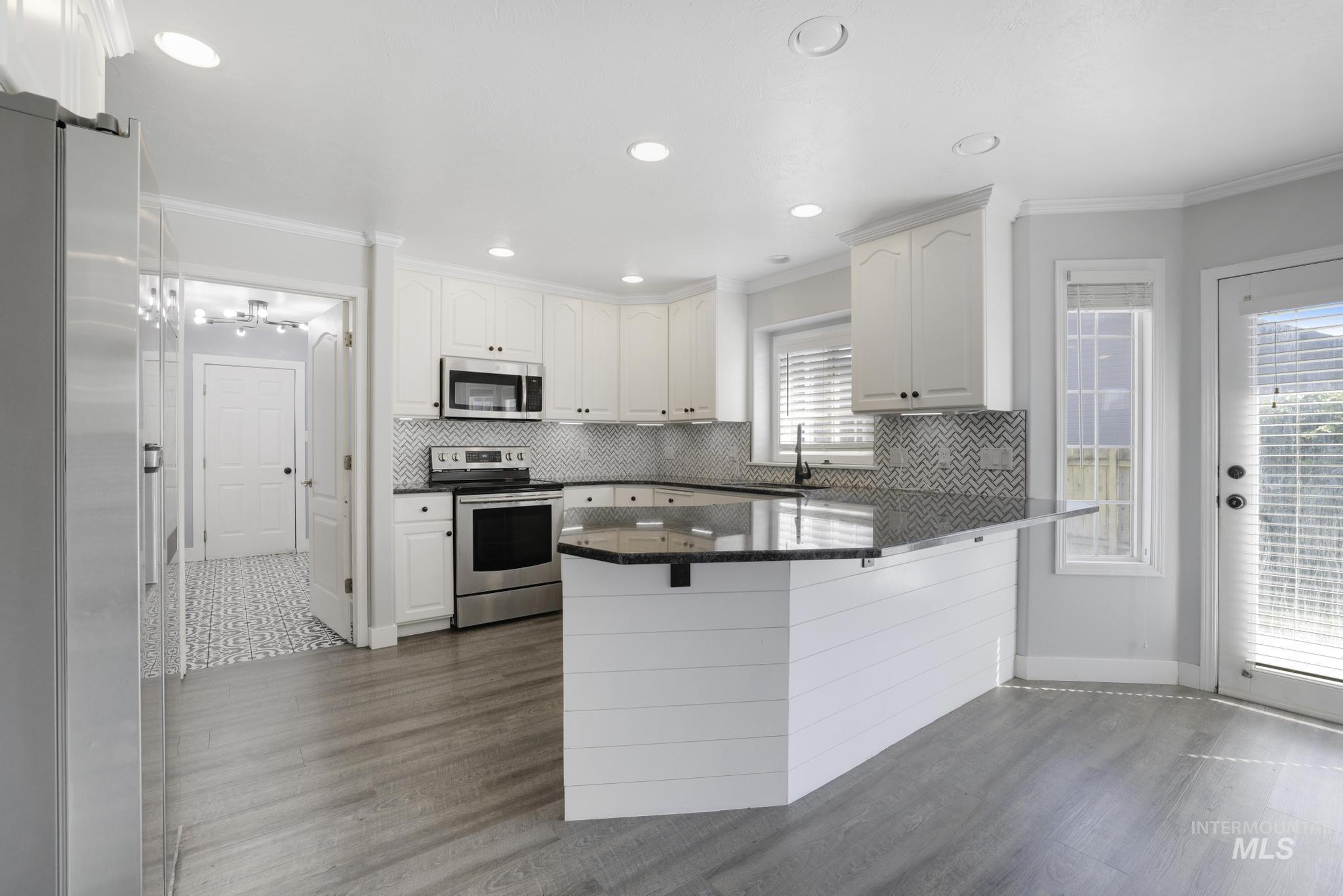 Kitchen featuring stainless steel appliances, ornamental molding, a peninsula, dark stone counters, and white cabinets
