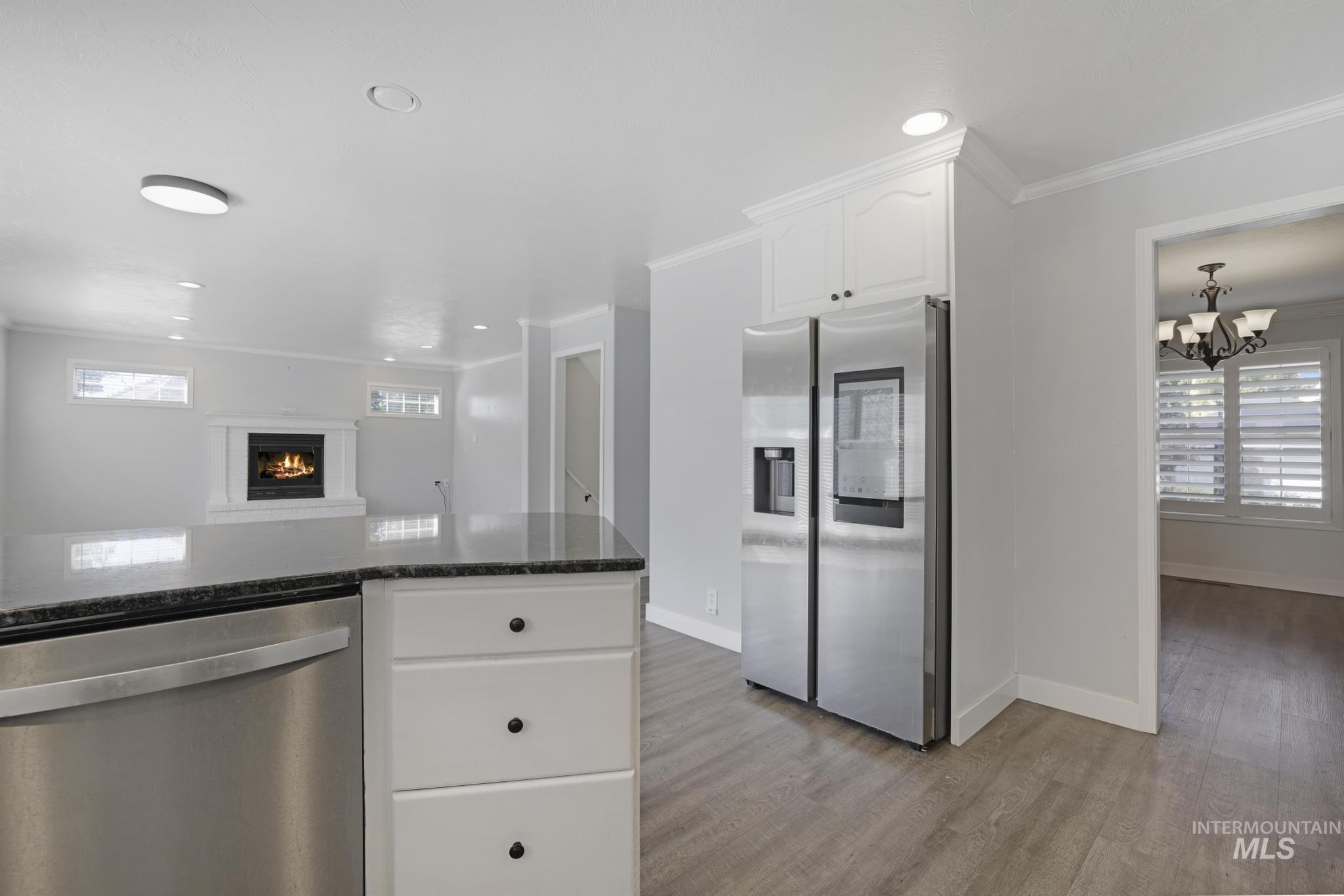 Kitchen featuring stainless steel appliances, white cabinetry, dark stone countertops, light wood-style flooring, and a chandelier
