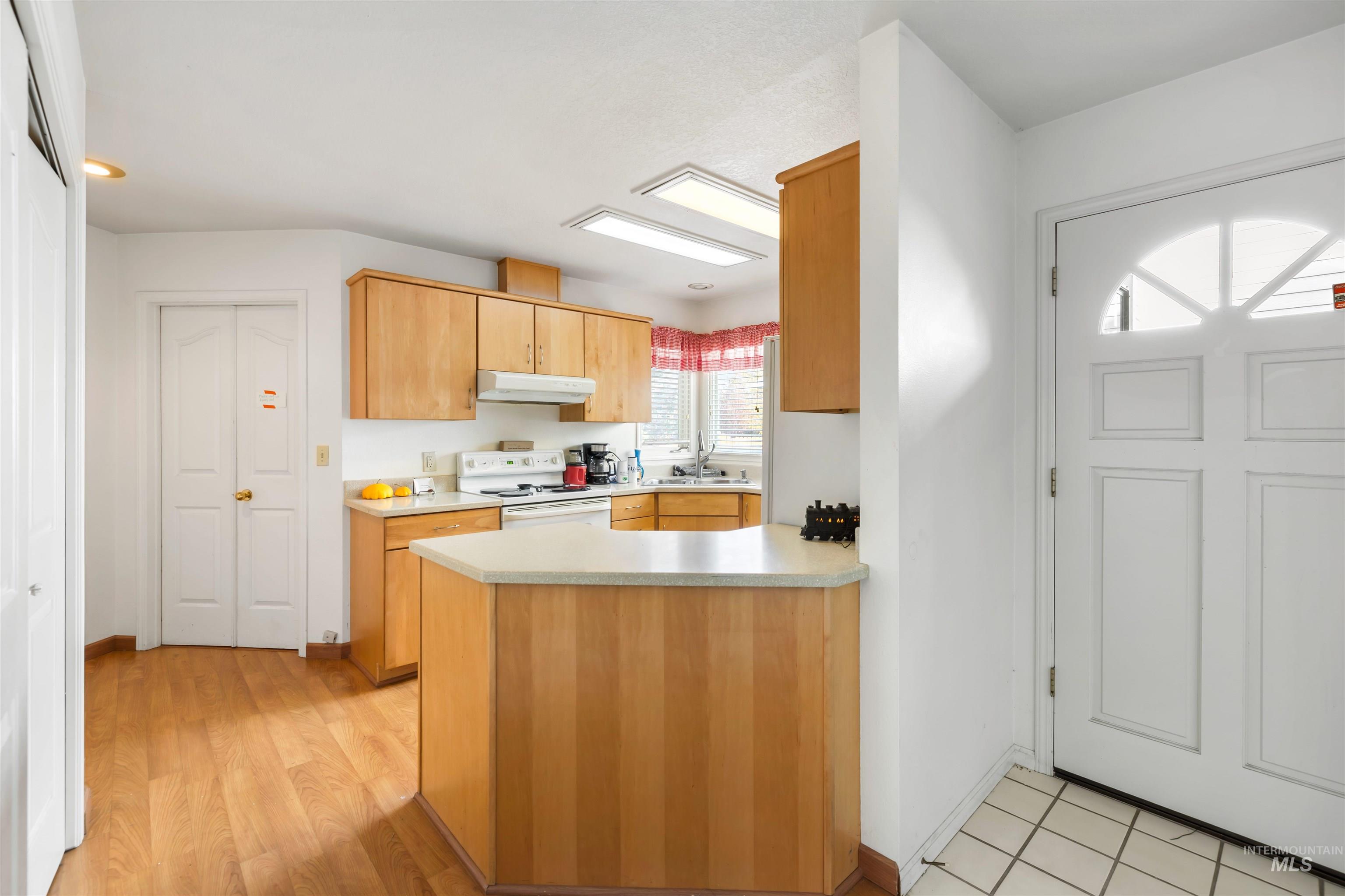 Kitchen with a peninsula, light countertops, electric stove, under cabinet range hood, and light wood-type flooring