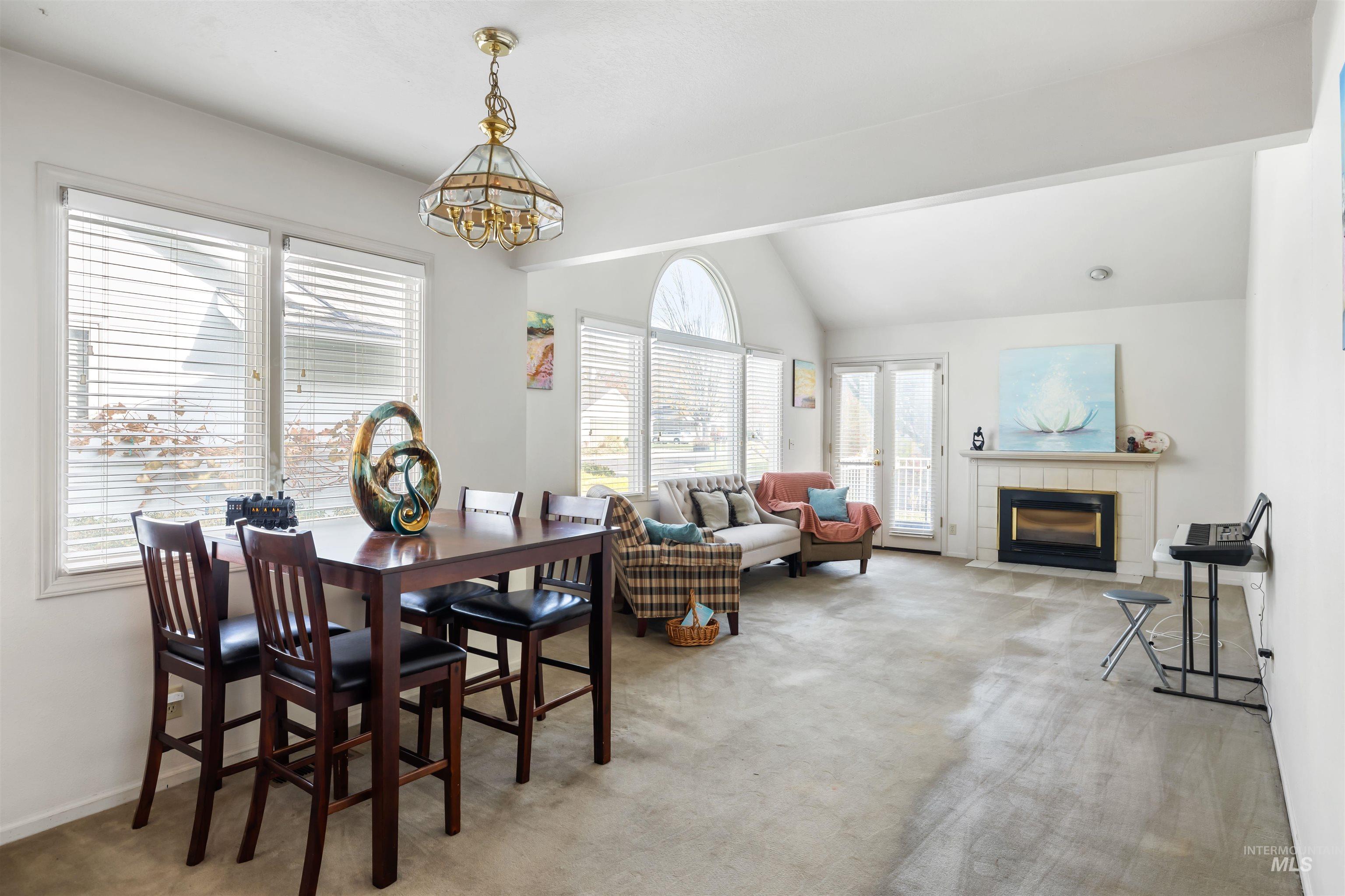 Dining area featuring light carpet, vaulted ceiling, a fireplace, and a chandelier