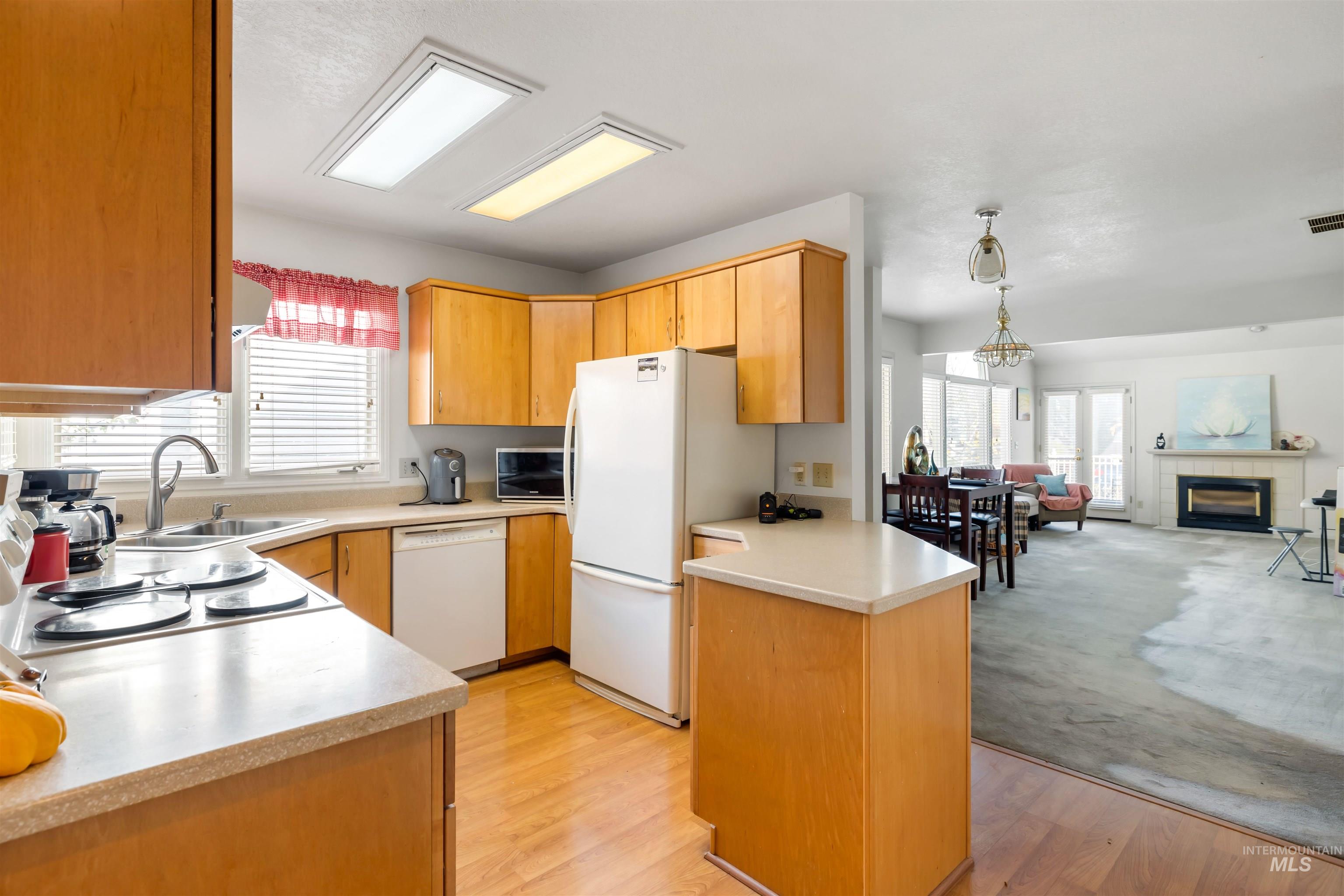 Kitchen featuring open floor plan, light countertops, white appliances, a peninsula, and a tile fireplace