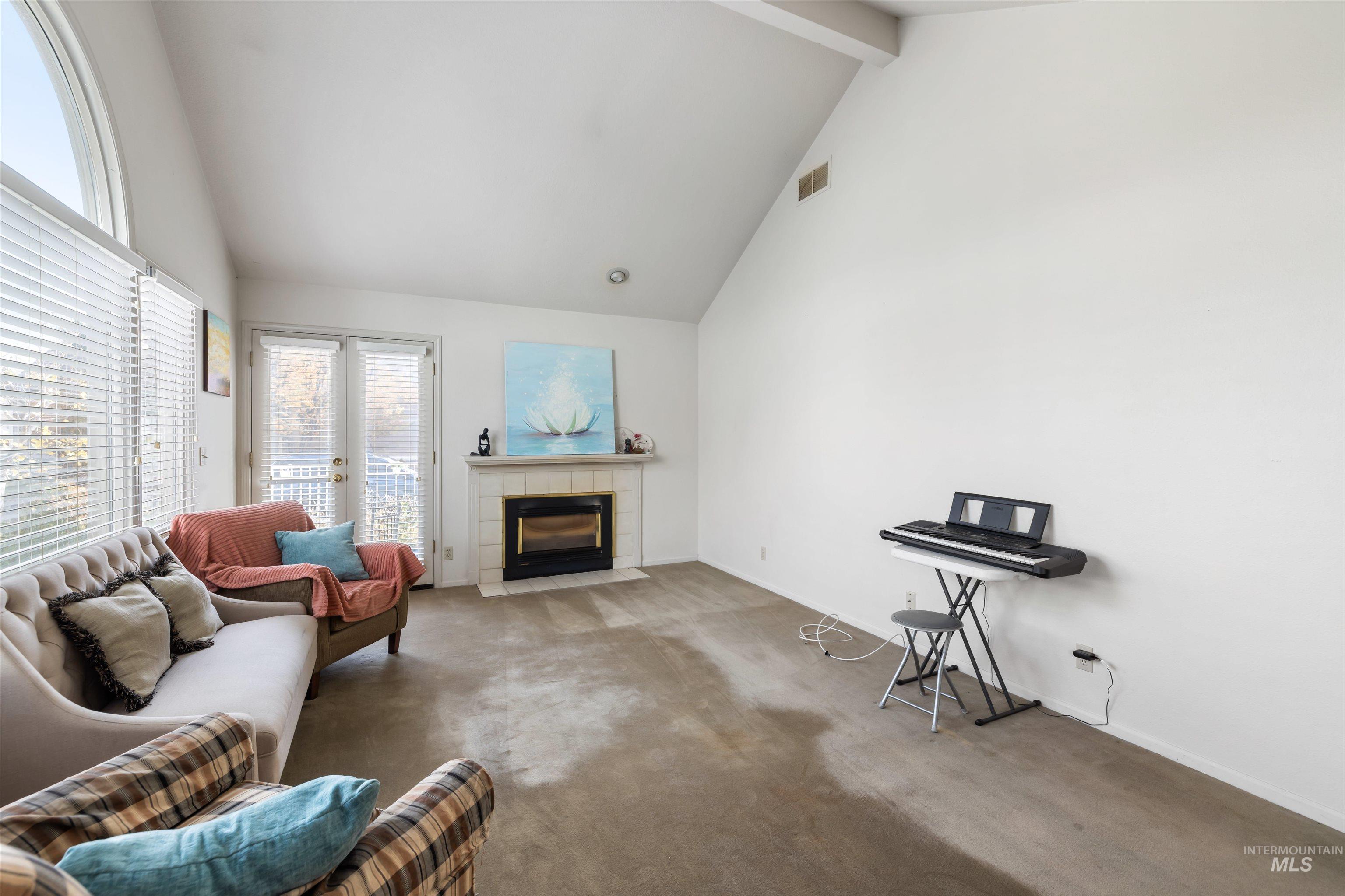 Carpeted living room featuring a fireplace, high vaulted ceiling, and beam ceiling