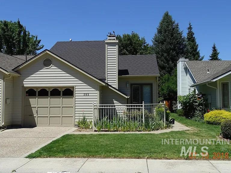 View of front facade with a chimney, a shingled roof, a front yard, a garage, and driveway