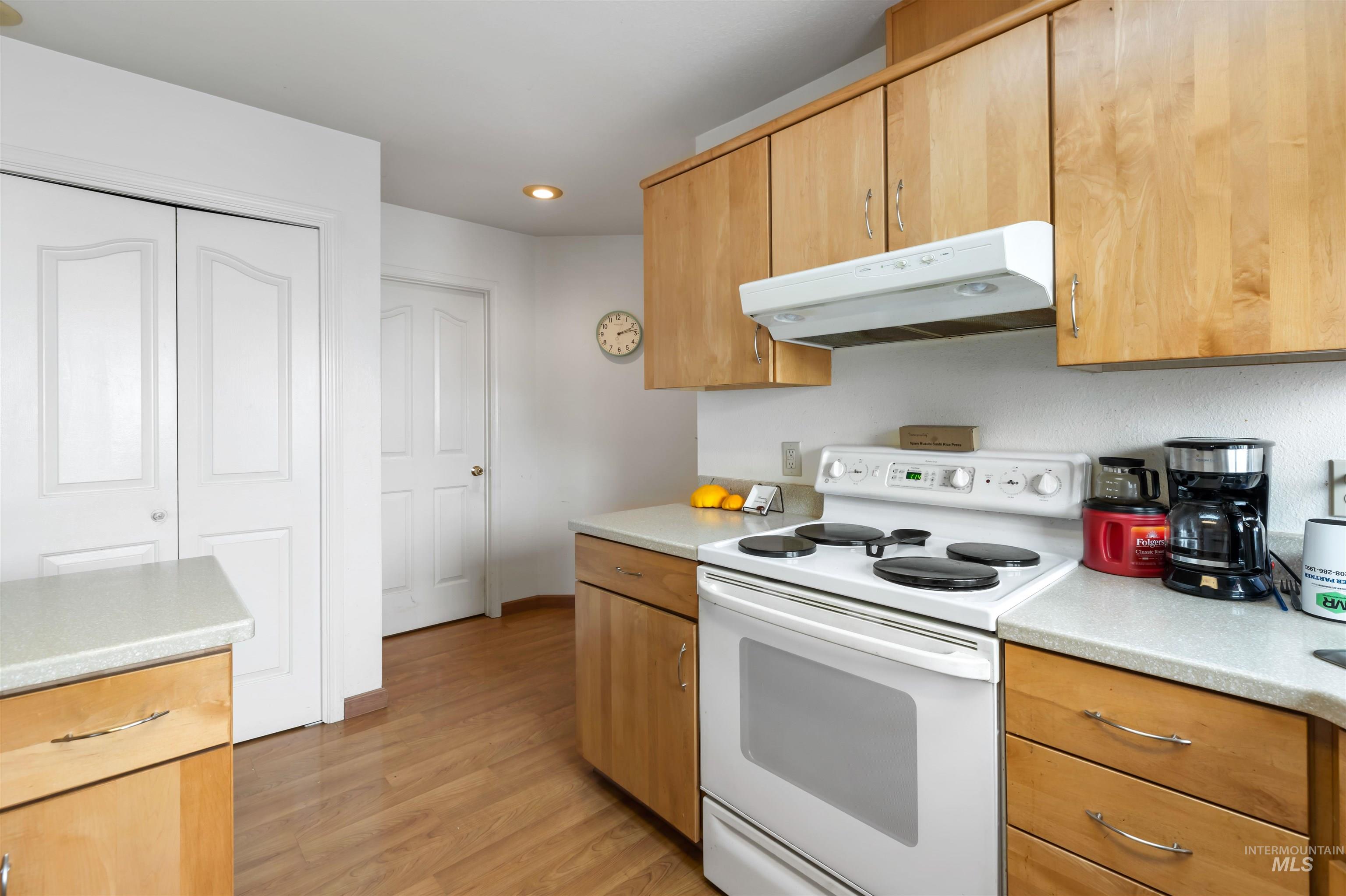Kitchen featuring white range with electric stovetop, under cabinet range hood, light wood finished floors, and recessed lighting