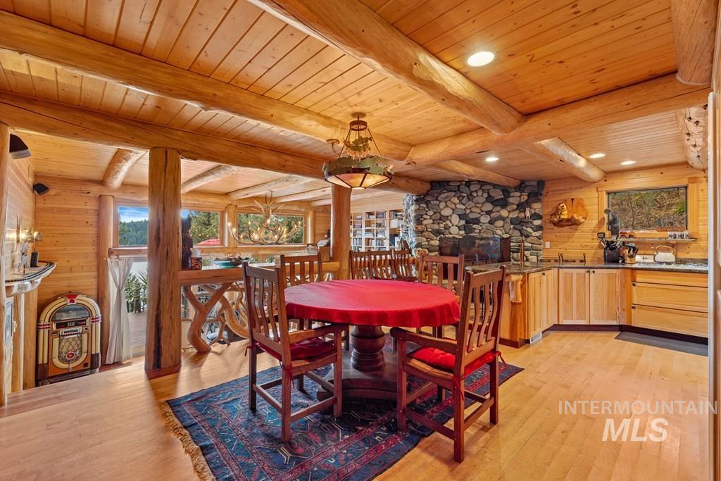 Expansive open-concept living area featuring a stone fireplace, wood-plank ceilings, natural wood walls and beams, and wood-finish flooring