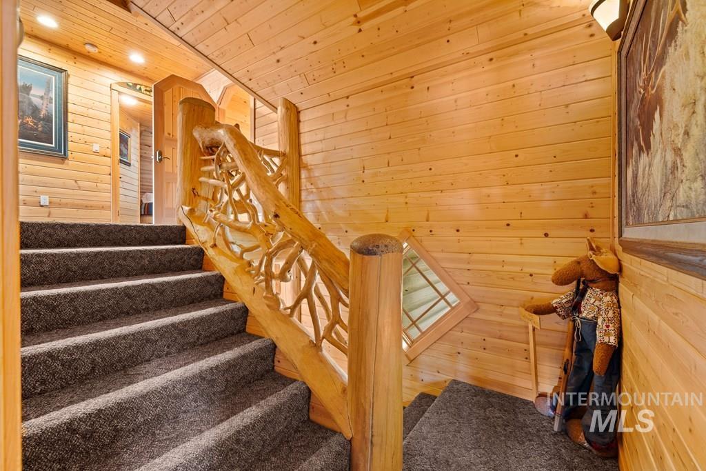 Carpeted staircase featuring a unique wood branch-style railing, natural wood plank walls, and integrated ceiling lighting