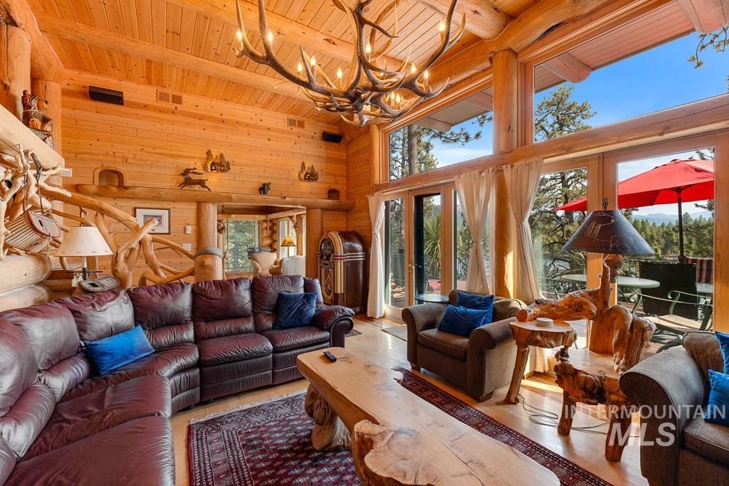 Spacious living area featuring extensive wood paneling and log beam construction, high ceilings, large windows, and light wood-finish flooring