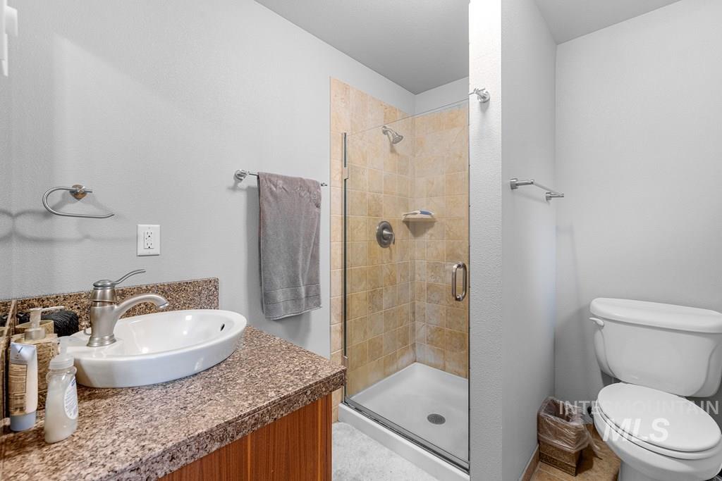 Bathroom featuring a wood-finish vanity with a speckled countertop, a white vessel sink with a brushed nickel faucet, and a tiled shower with a glass enclosure