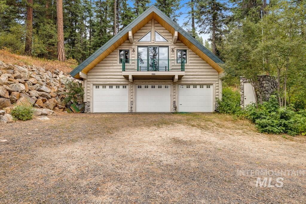 Log cabin exterior featuring an A-frame roofline, a three-car garage, and a second-story balcony with metal railing