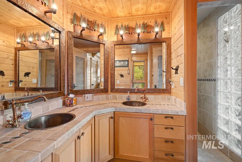 Double vanity featuring copper vessel sinks, tiled countertops with decorative accents, and natural wood cabinetry
