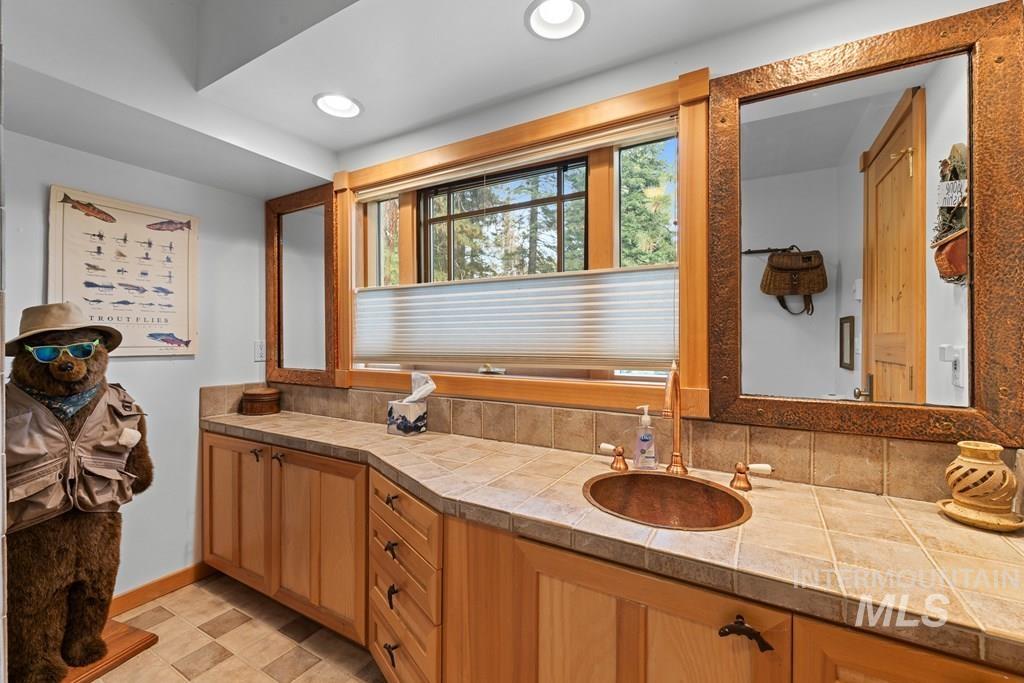 Rustic vanity featuring a copper basin sink, tile countertop, and wood-finish cabinetry