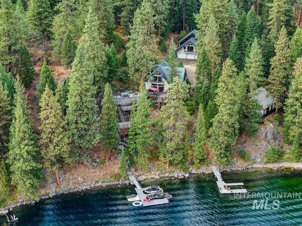 Waterfront property featuring multiple structures, mature evergreen trees, private dock access, a boat lift, and a rocky shoreline