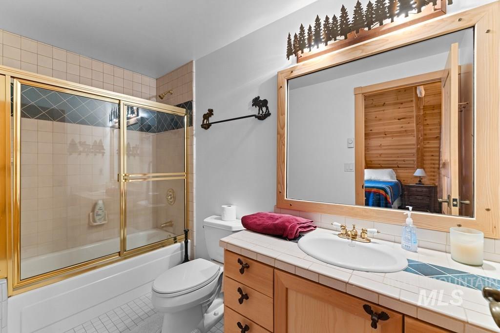 Bathroom featuring a full-size bathtub with gold-toned sliding glass shower doors, a tiled vanity with an integrated sink, a wood-framed mirror, and a decorative overhead light fixture
