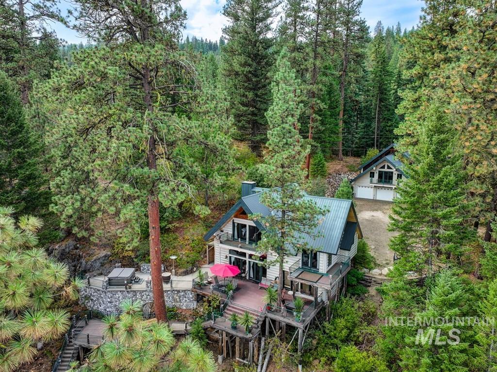 Multi-level property nestled among mature pine trees, featuring multiple expansive decks, a hot tub area with stone retaining walls, and a detached structure with a multi-car garage