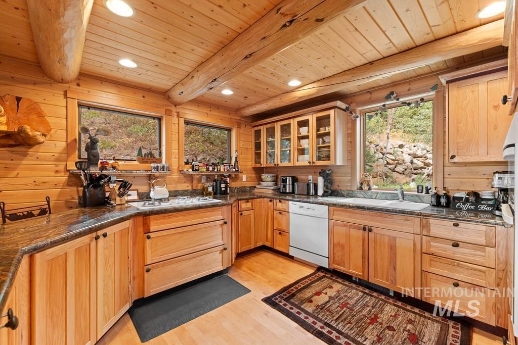 Log cabin-style kitchen featuring wood-paneled walls and ceiling, exposed wooden beams, and recessed lighting