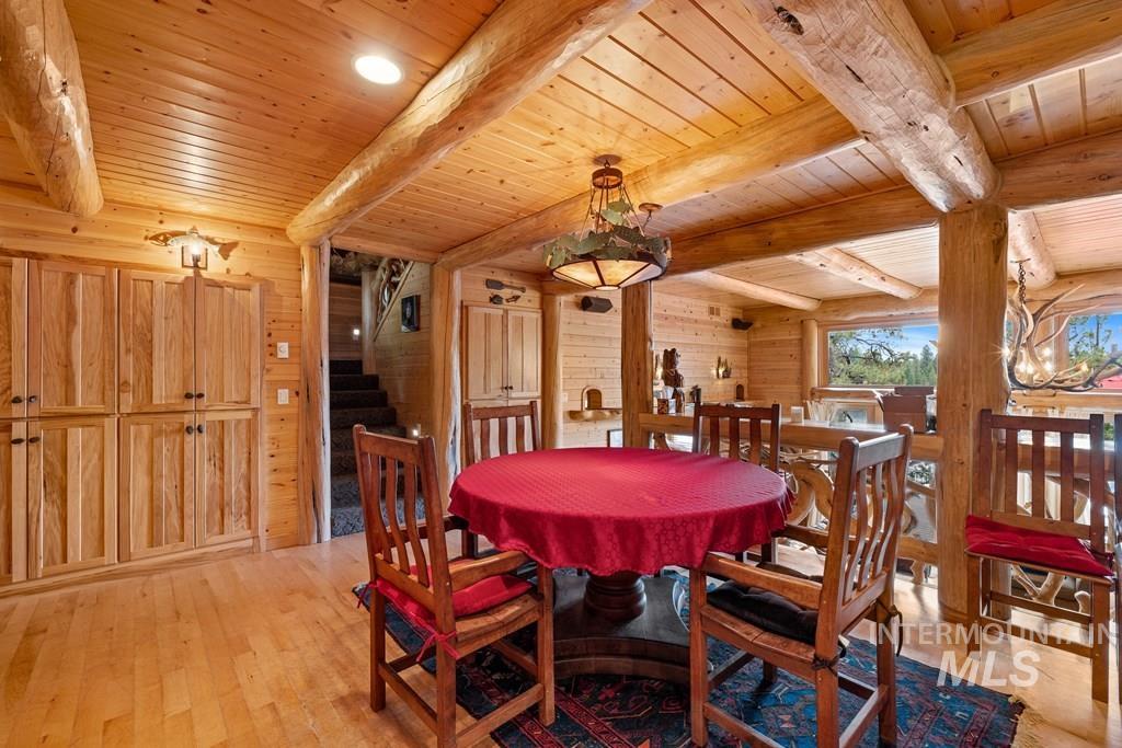 Open concept living space featuring extensive wood paneling, exposed log beams, wood-finish flooring, built-in cabinetry, and a unique chandelier