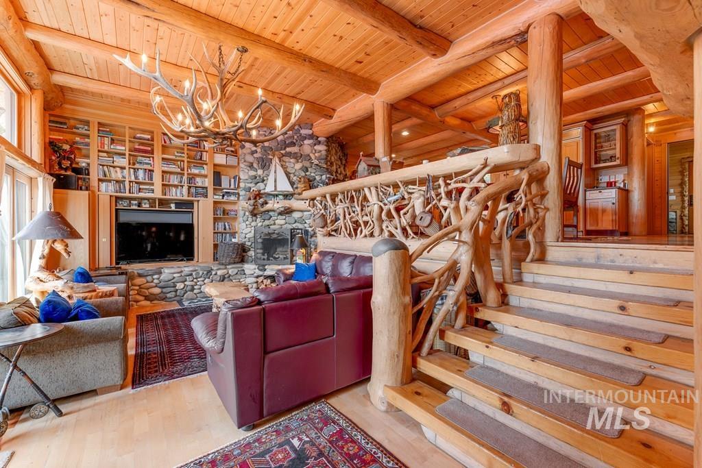 Inviting living space featuring a floor-to-ceiling stone fireplace, built-in shelving, natural wood-finish flooring, and a distinctive wooden staircase with a rustic railing