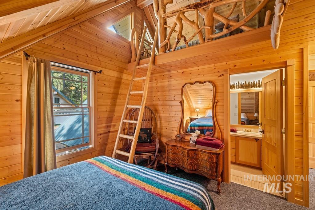 Pine wood-paneled bedroom featuring a lofted space, a ladder, a double-hung window, and an open doorway revealing a bathroom with a vanity