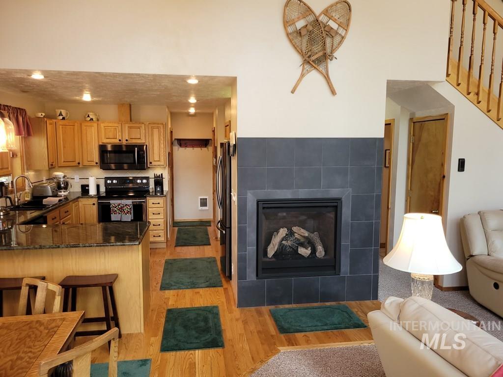 Kitchen featuring dark stone countertops, black appliances, a tile fireplace, light wood-style flooring, and a peninsula