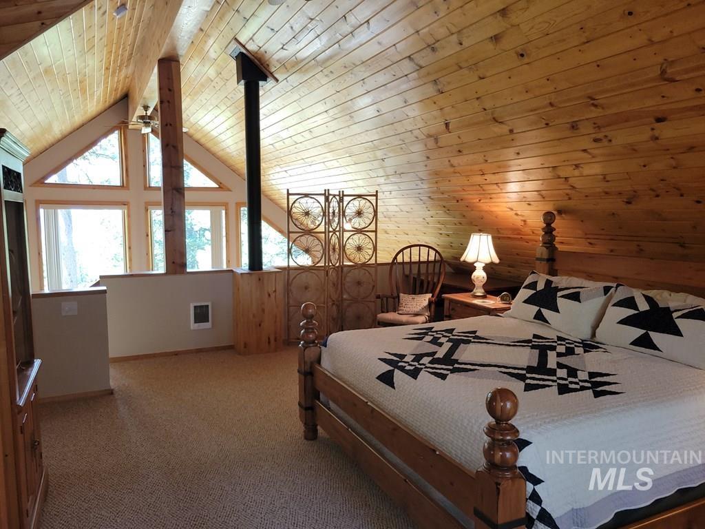 Bedroom with a wooden ceiling with exposed beams, carpet, wood walls, and high vaulted ceiling