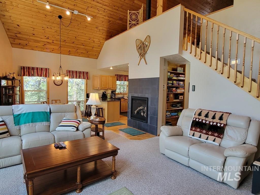 Living area with wooden ceiling, a tiled fireplace, high vaulted ceiling, rail lighting, and a chandelier