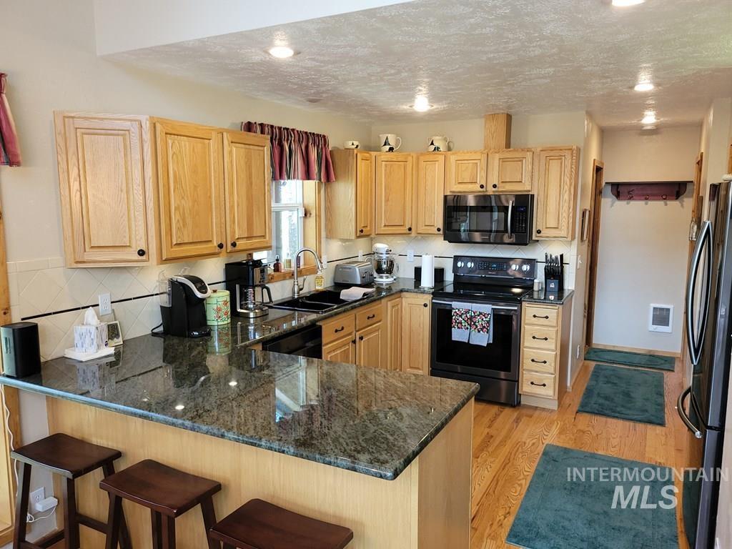 Kitchen with black appliances, decorative backsplash, a peninsula, light wood-style flooring, and a textured ceiling