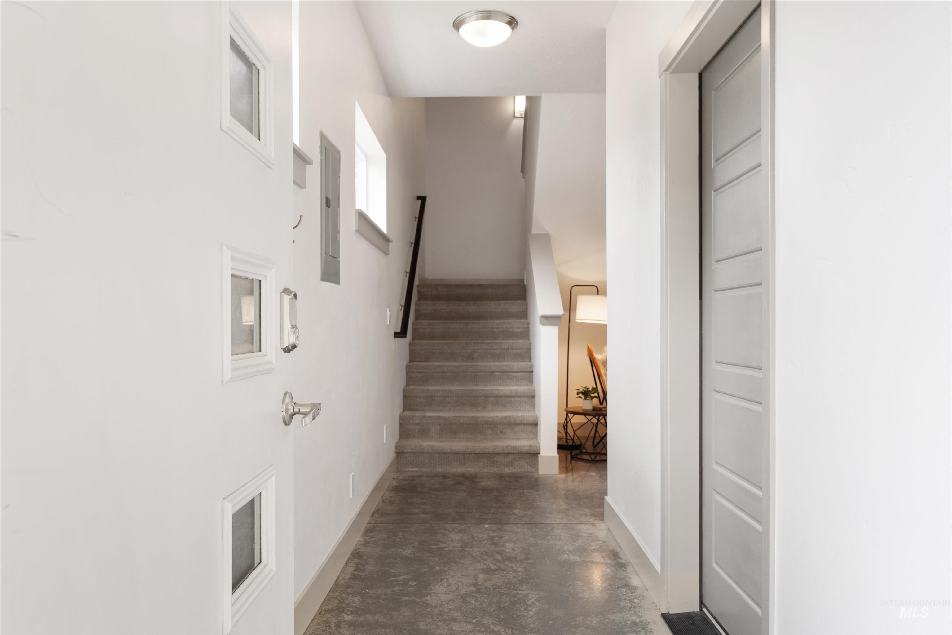 Entryway featuring polished concrete flooring, a modern panel door, and a staircase with a black handrail
